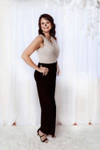 Photo of Tina Hodgdon dressed nicely during her 40 over 40 photo shoot. She is wearing blank pants, silver sparkle top, black heels and white background